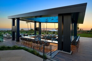 Un espace bar extérieur avec vue sur la piscine, des tabourets de bar et une piscine où nagent des poissons.