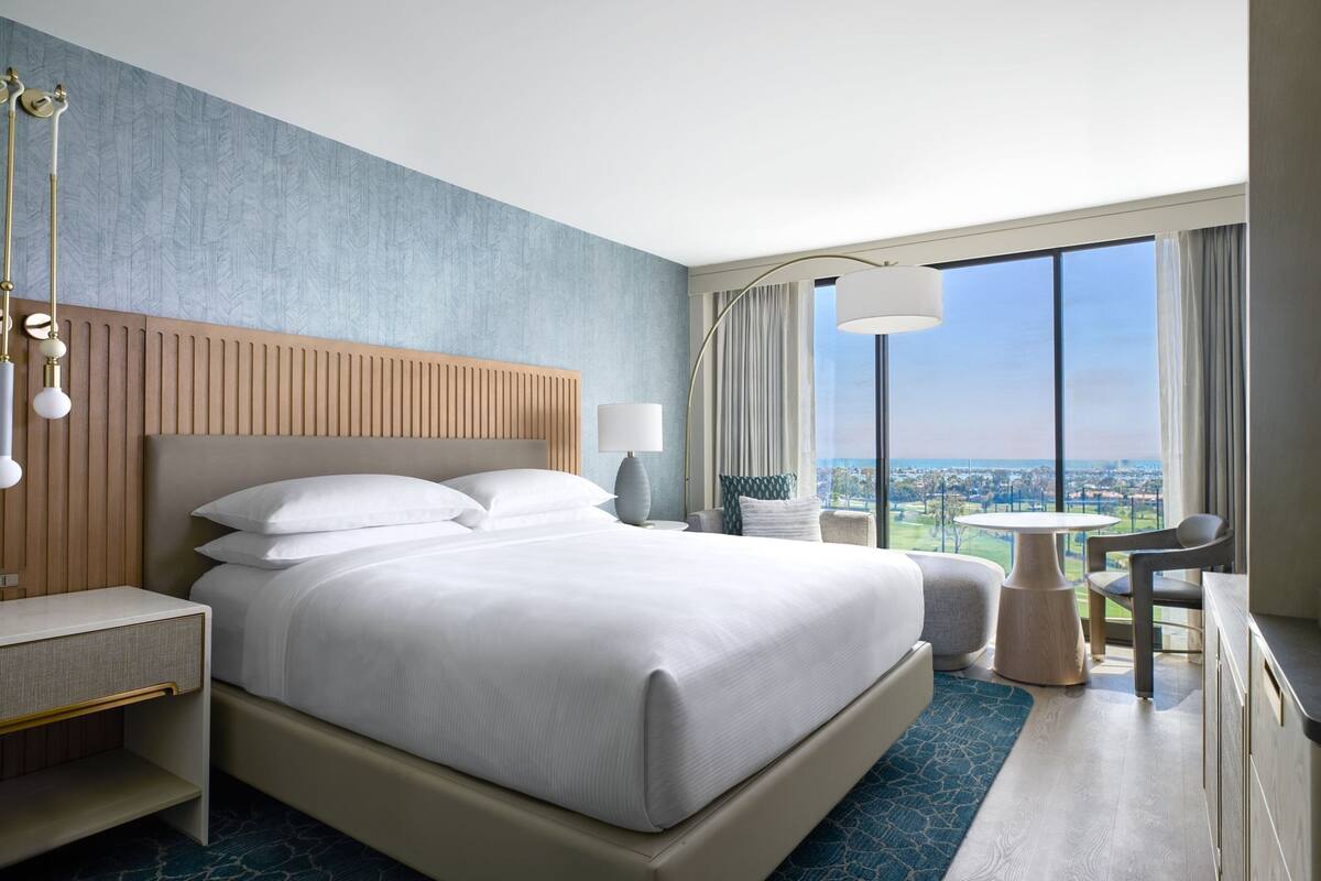 Una habitación de hotel moderna con una cama grande, un escritorio, una silla, una mesa y vistas a la ciudad.