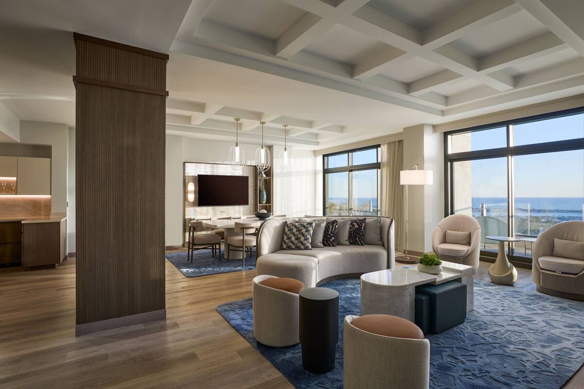 Una sala moderna con un sofá modular, una mesa de centro y un televisor. Una ventana grande ofrece vistas al océano.