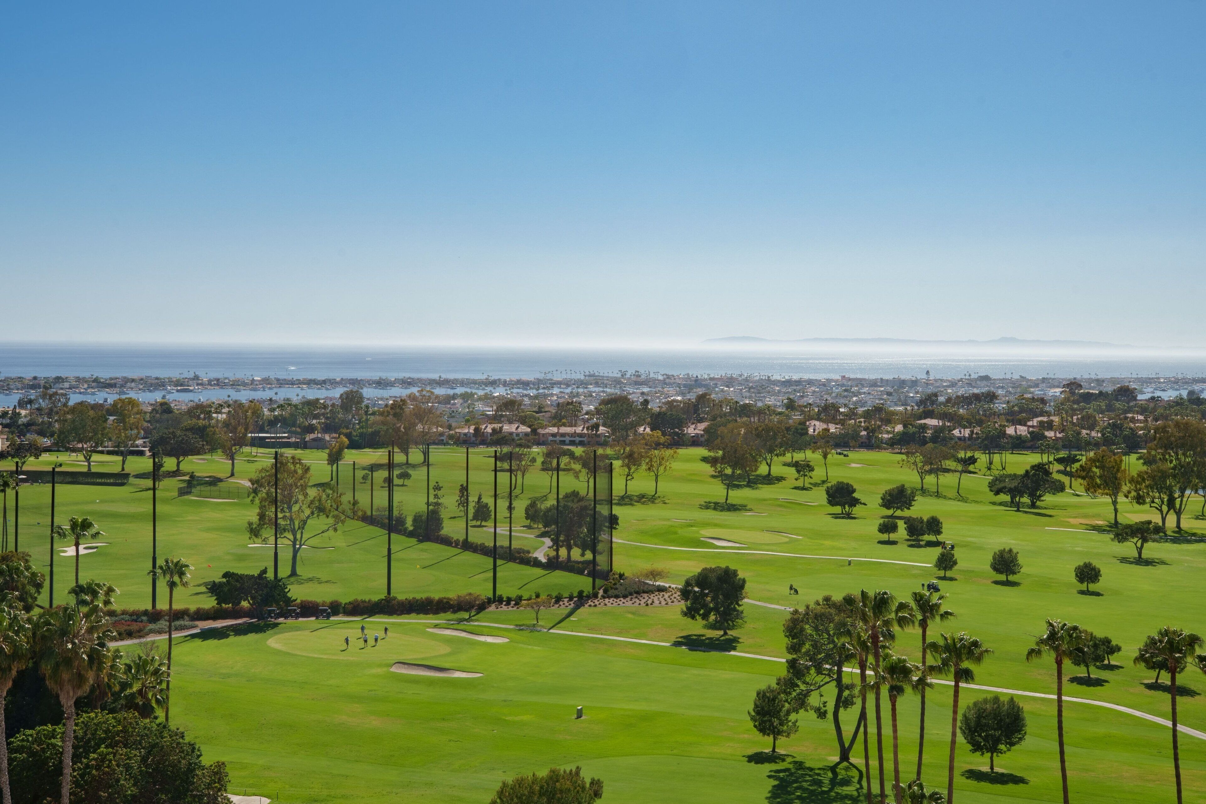 A golf course with a clear view of the ocean and cityscape in the background.