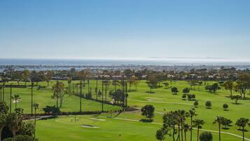 A golf course with a clear view of the ocean and cityscape in the background.