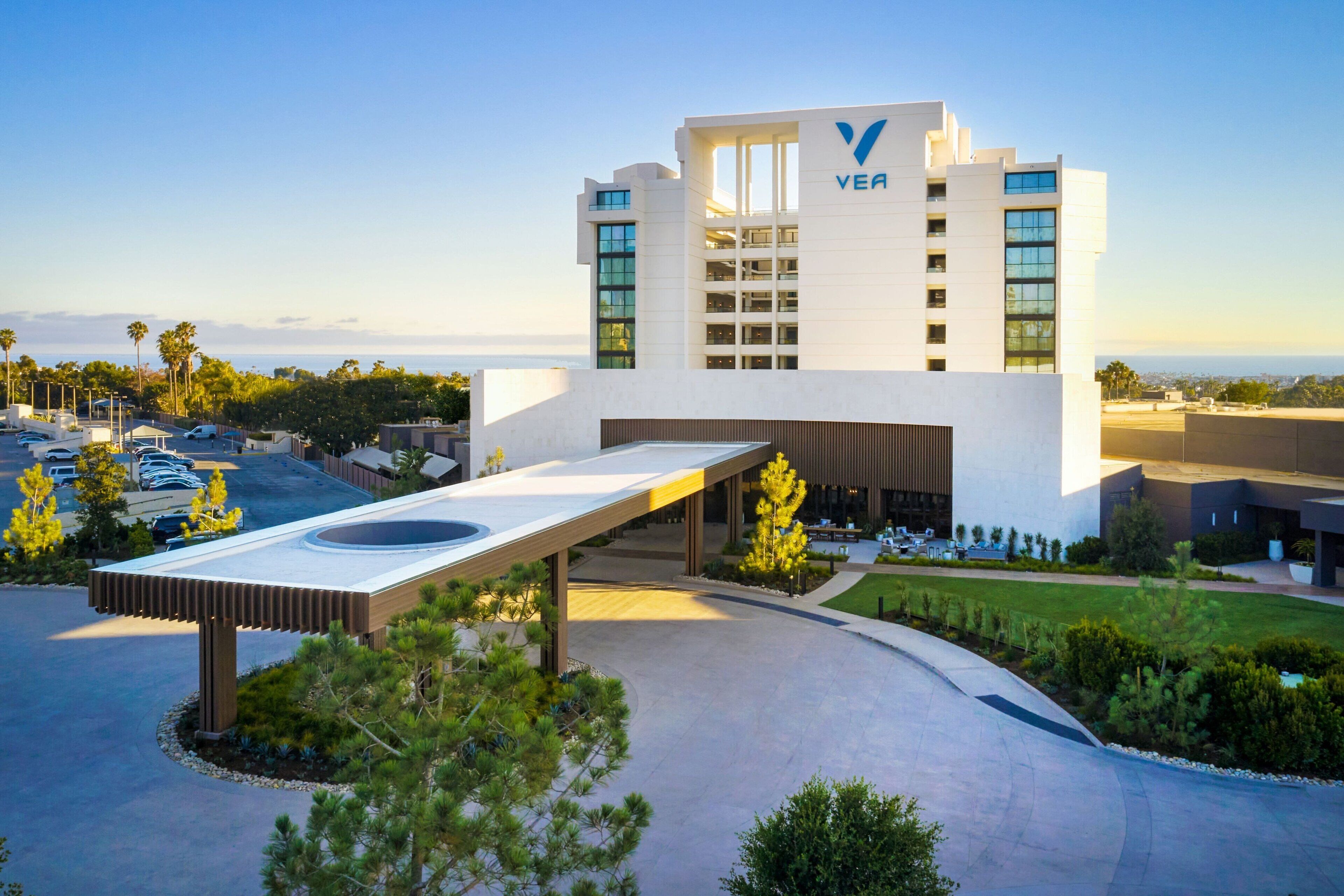 A modern hotel with a prominent VEA logo, a covered outdoor area, and a parking lot.