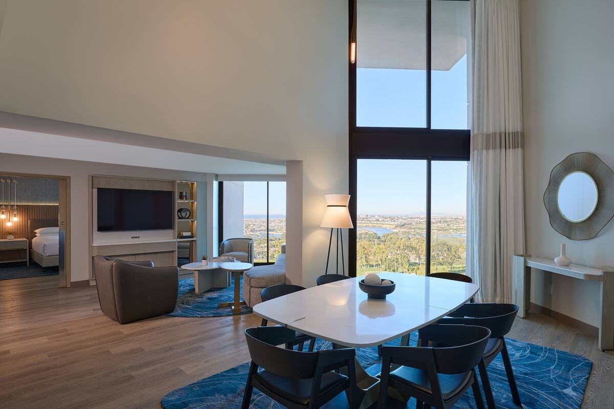 Una habitación de hotel moderna con comedor, televisor, sofá y vistas a la ciudad.