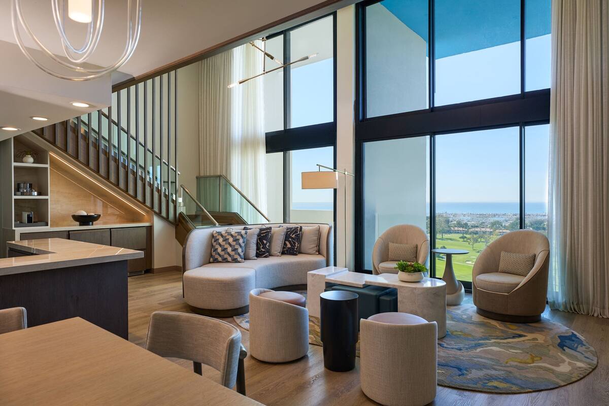 Amplia sala de estar con un gran ventanal, una escalera y una cocina moderna.