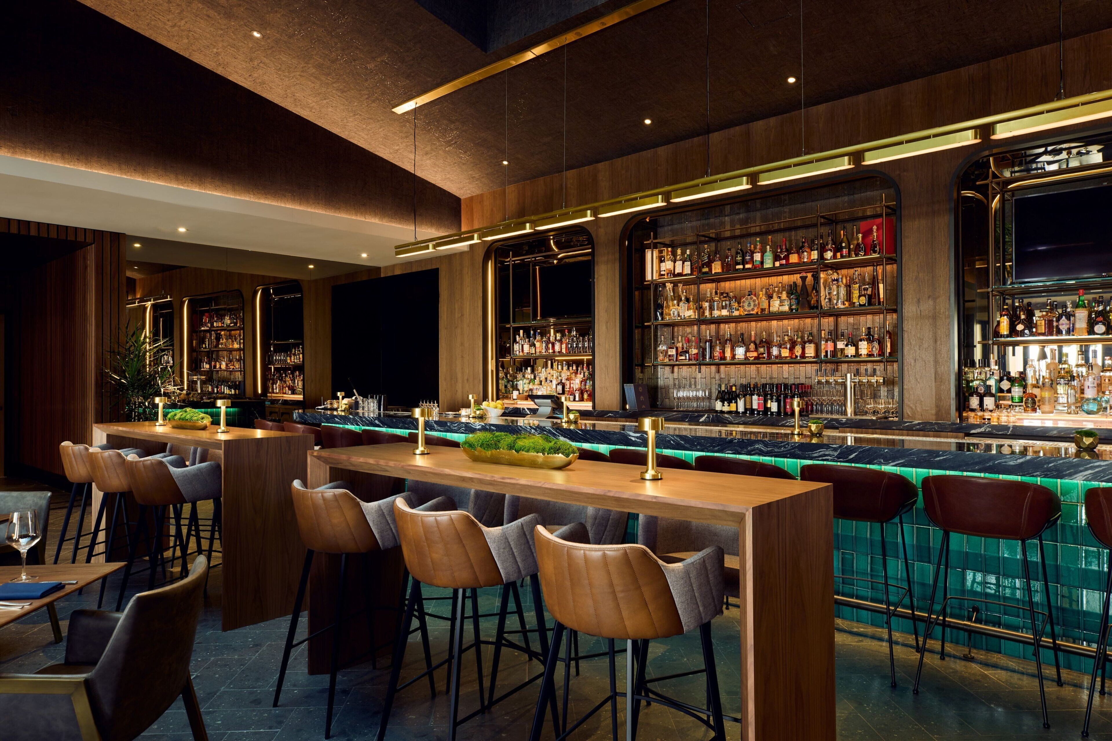 A bar area with wooden bar counters, stools, and shelves of bottles.