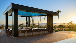 Un espace bar extérieur moderne, doté d’une piscine, de tabourets de bar et offrant une vue sur l’océan et les montagnes.