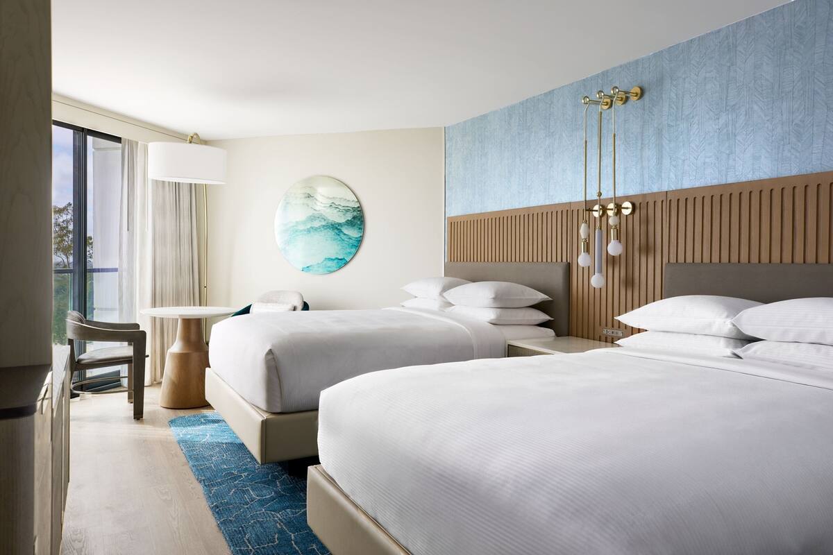 Habitación de hotel con dos camas, una mesa redonda, una silla y un ventanal grande.