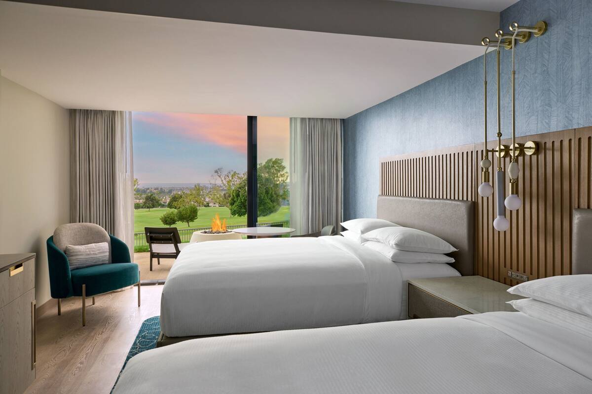 Una habitación de hotel con dos camas, un escritorio, una silla y vistas al exterior.