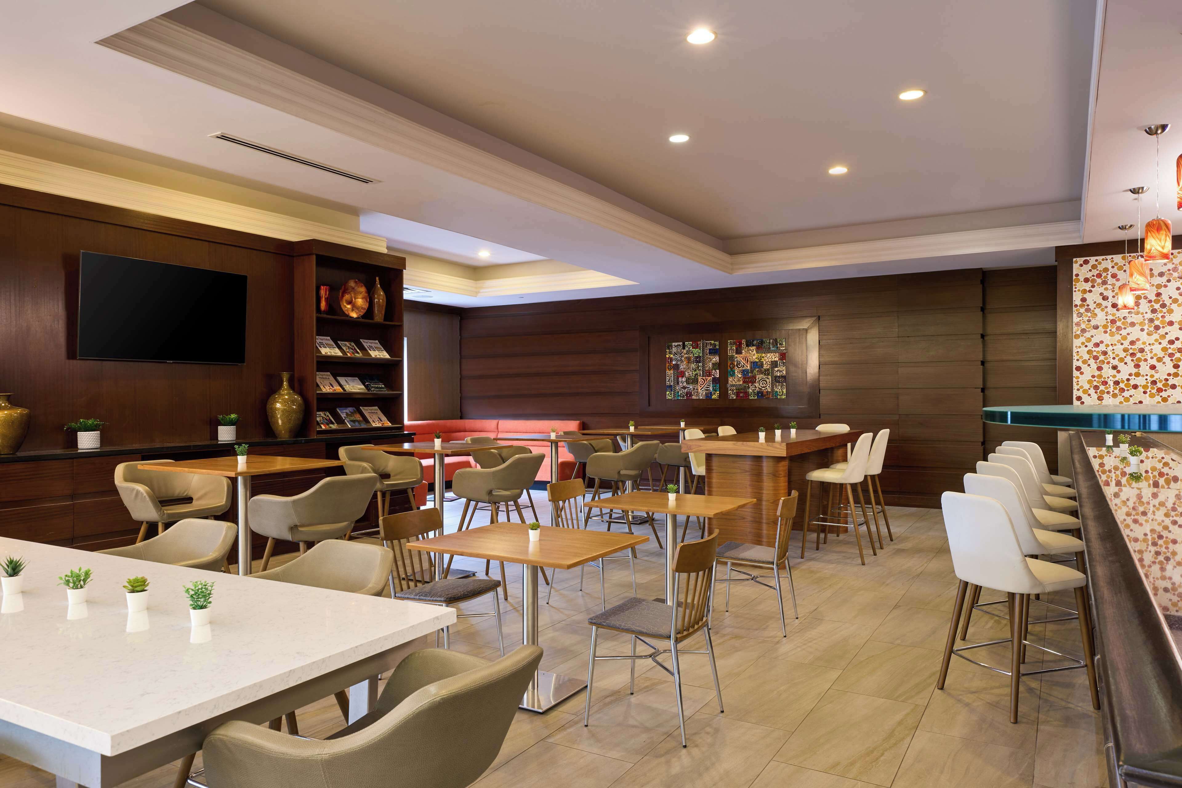 Un restaurante moderno con varias mesas y sillas, una zona de bar y un televisor de pantalla plana en la pared.