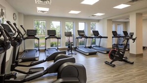 Un gimnasio con varias cintas de correr y bicicletas estáticas, ventanas amplias y un diseño limpio y moderno.