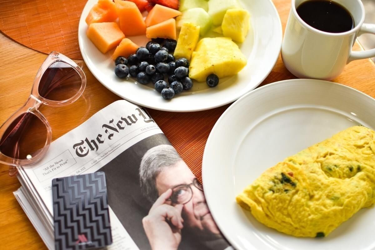 A breakfast setting with a plate of fruit, a cup of coffee, and an omelette on a table.