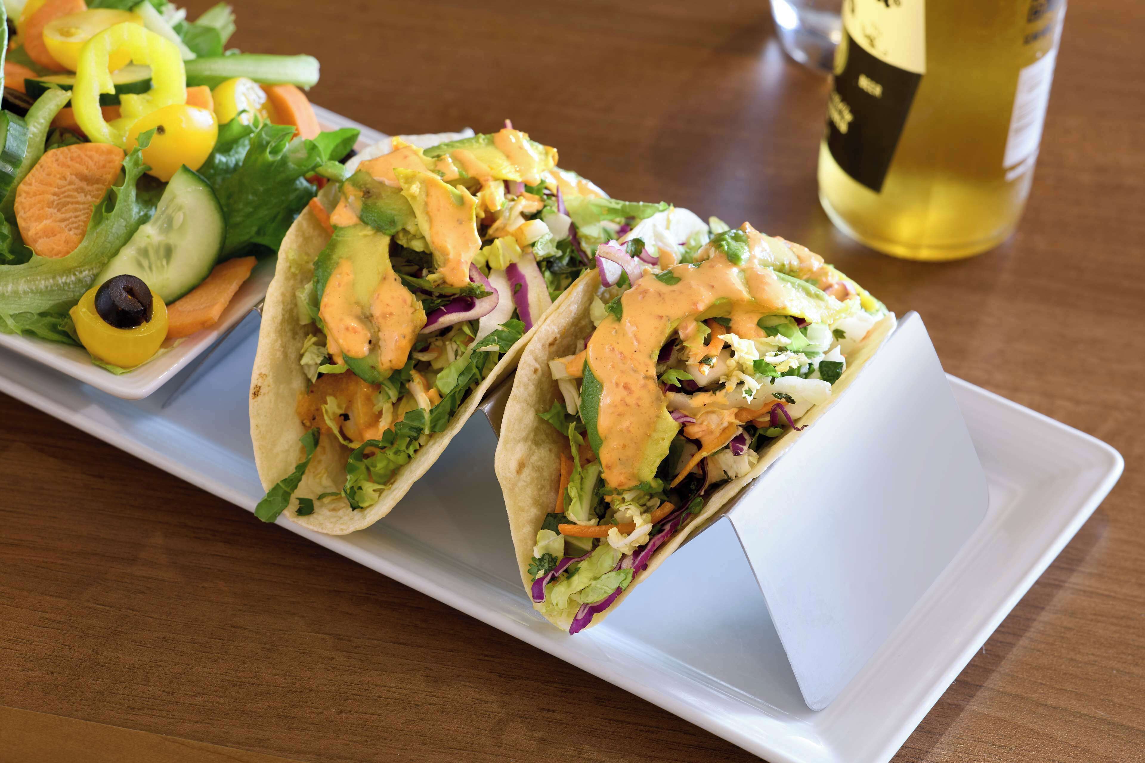 Dois tacos com uma salada e uma garrafa de vinho branco sobre uma mesa de madeira.