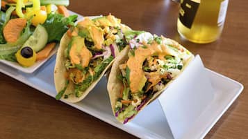 Dois tacos com uma salada e uma garrafa de vinho branco sobre uma mesa de madeira.