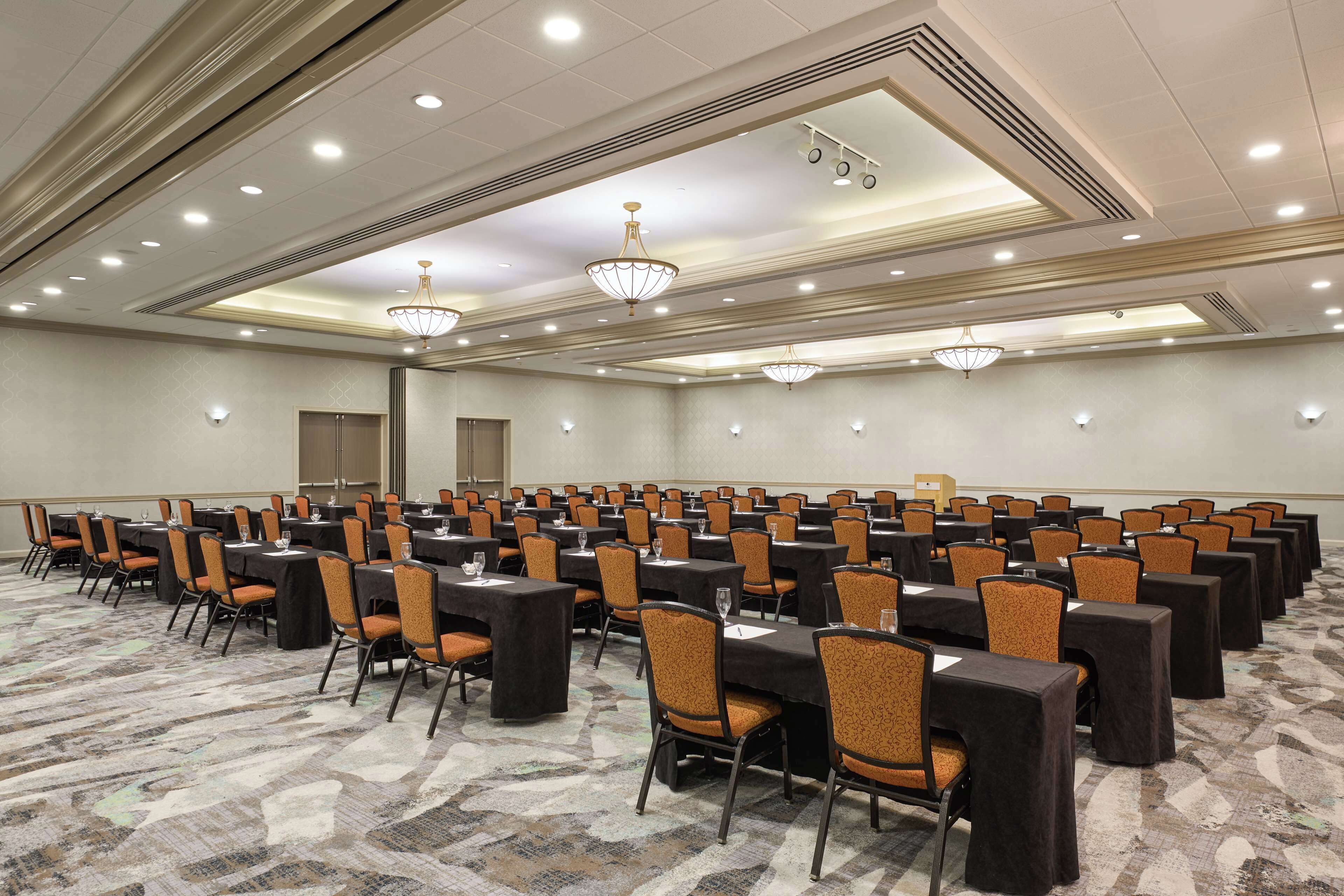 Sala de conferência com fileiras de mesas e cadeiras, equipada com placas de identificação e copos d'água.