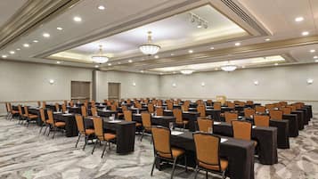 Sala de conferência com fileiras de mesas e cadeiras, equipada com placas de identificação e copos d'água.