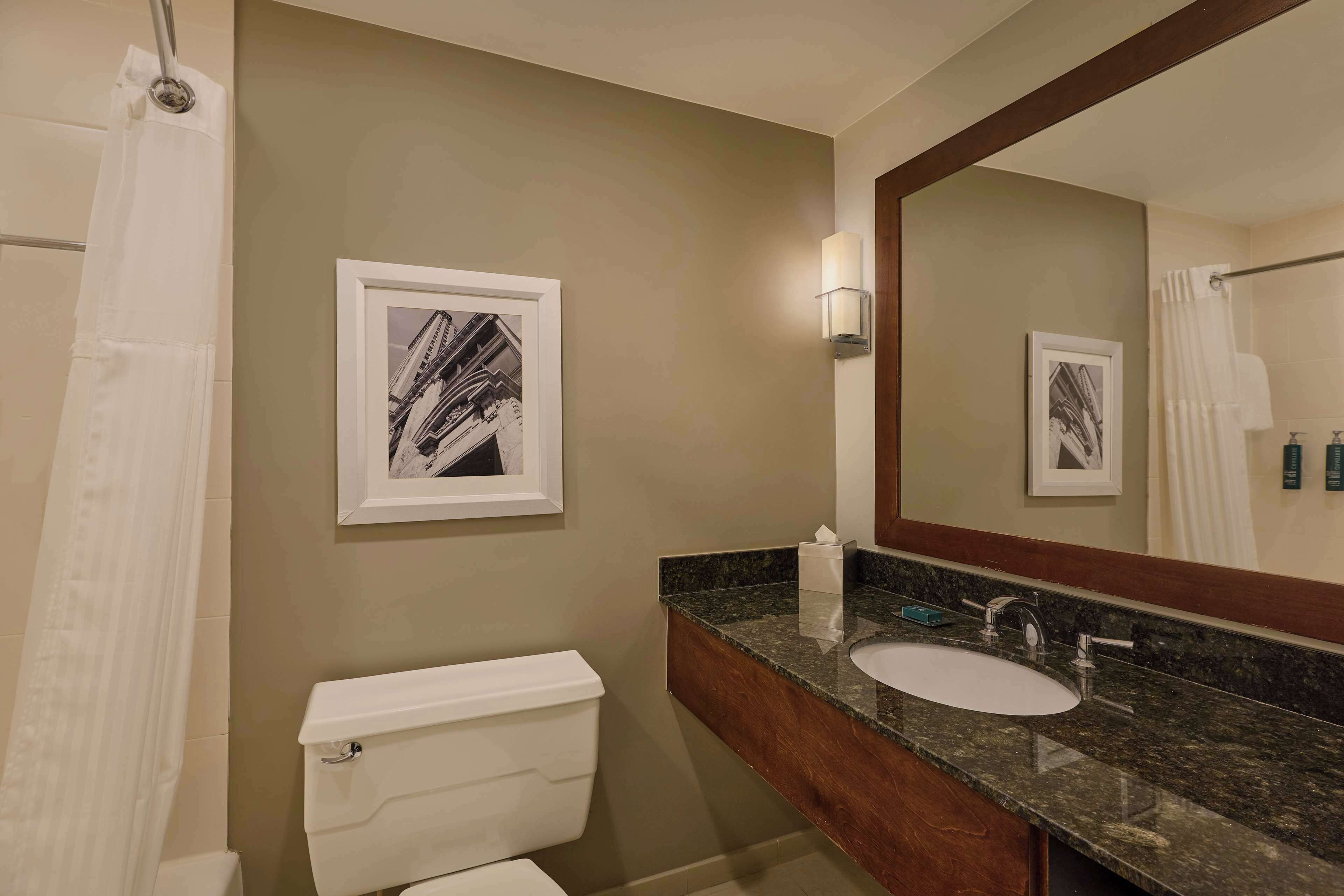 A bathroom with a toilet, sink, and a large mirror. There are framed pictures on the wall and a shower curtain.