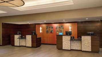 Un hall d'accueil d'hôtel avec deux comptoirs de réception, un mur décoratif orné d'une enseigne « Hilton » et un lustre moderne.