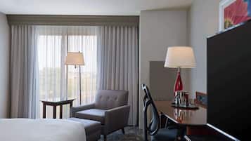 Habitación de hotel con cama, escritorio con lámpara, silla, televisión y ventana con cortinas.
