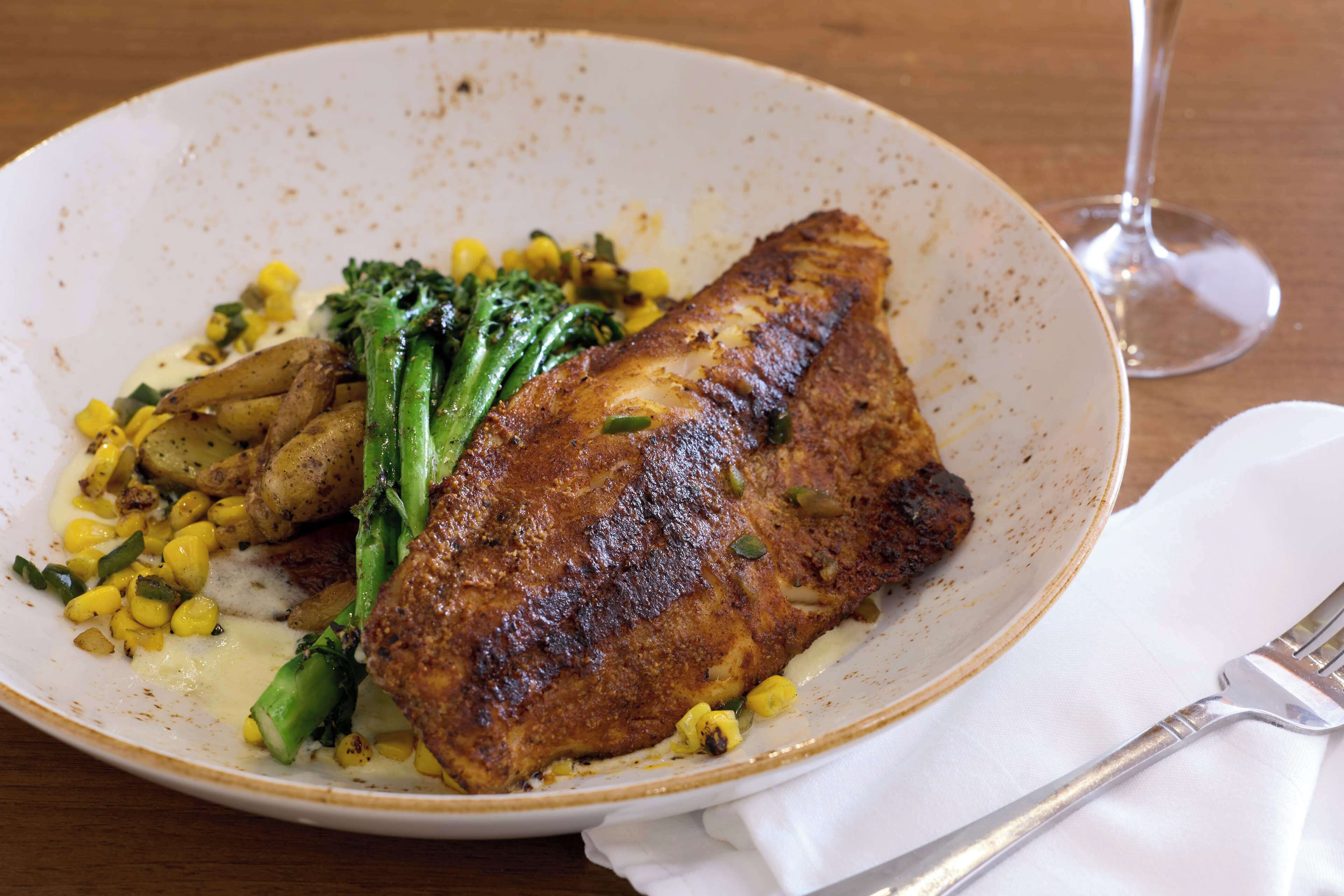 A plate with a piece of grilled meat, vegetables, and a glass of wine on a wooden table.