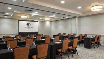A conference room with multiple tables and chairs, a projector screen displaying the DoubleTree by Hilton logo, and a carpeted floor.