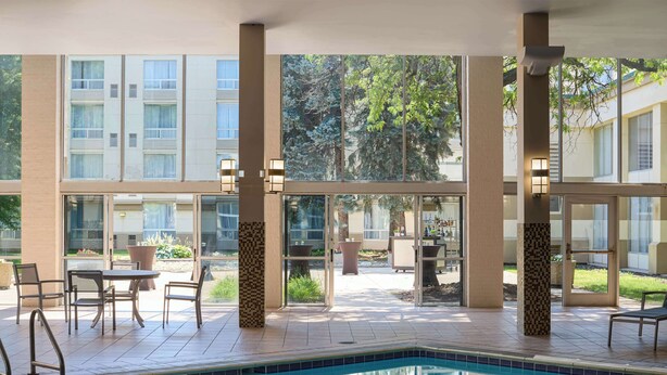 Una zona de piscina con vistas a un edificio con múltiples ventanales y un patio con mobiliario exterior.