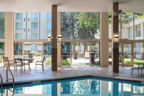 A pool area with a view of a building with multiple windows and a patio with outdoor furniture. - DoubleTree by Hilton Minneapolis Airport, MN (Bloomington)