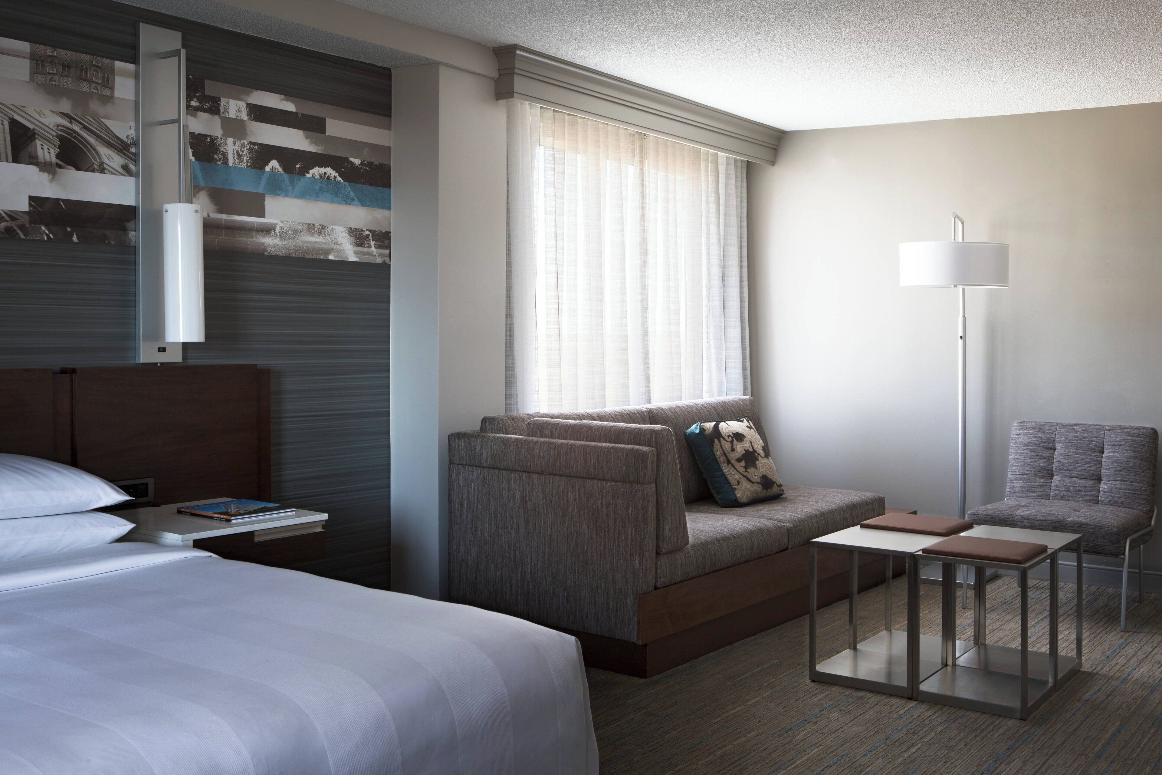 A modern hotel room with a bed, a sofa, a small table, and a chair.