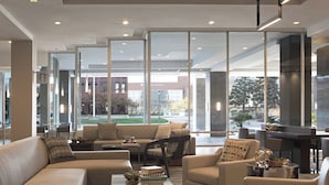 A modern hotel lobby with a large seating area, a coffee table, and a view of the outside.
