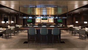 A modern bar area with a long counter, bar stools, and a television screen.