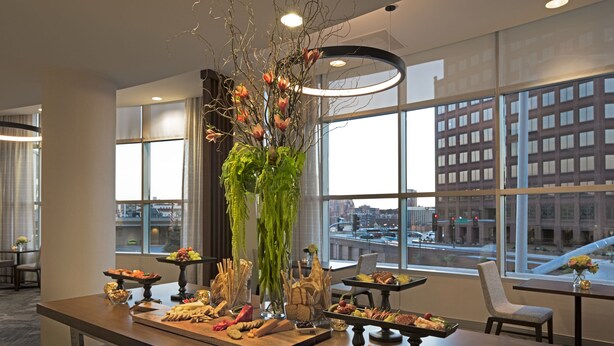 A modern hotel lobby with a long reception counter displaying various food items and a large vase with flowers.