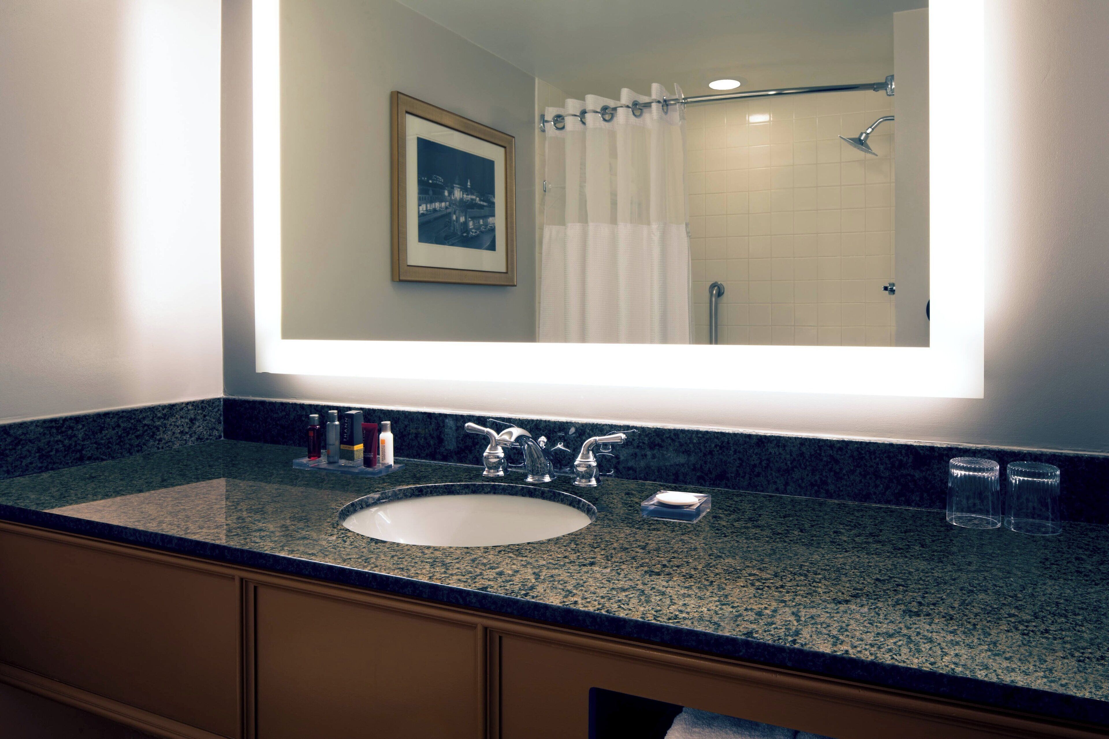 A bathroom with a large mirror, a sink, and a shower.