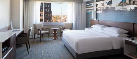 A hotel room with a bed, a desk, two chairs, a small table, and a window with curtains.