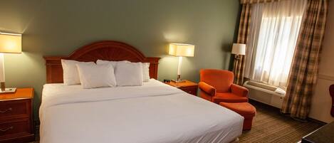 Quarto de hotel com uma cama grande, duas mesas de cabeceira com abajures, uma cadeira e uma janela com cortinas.