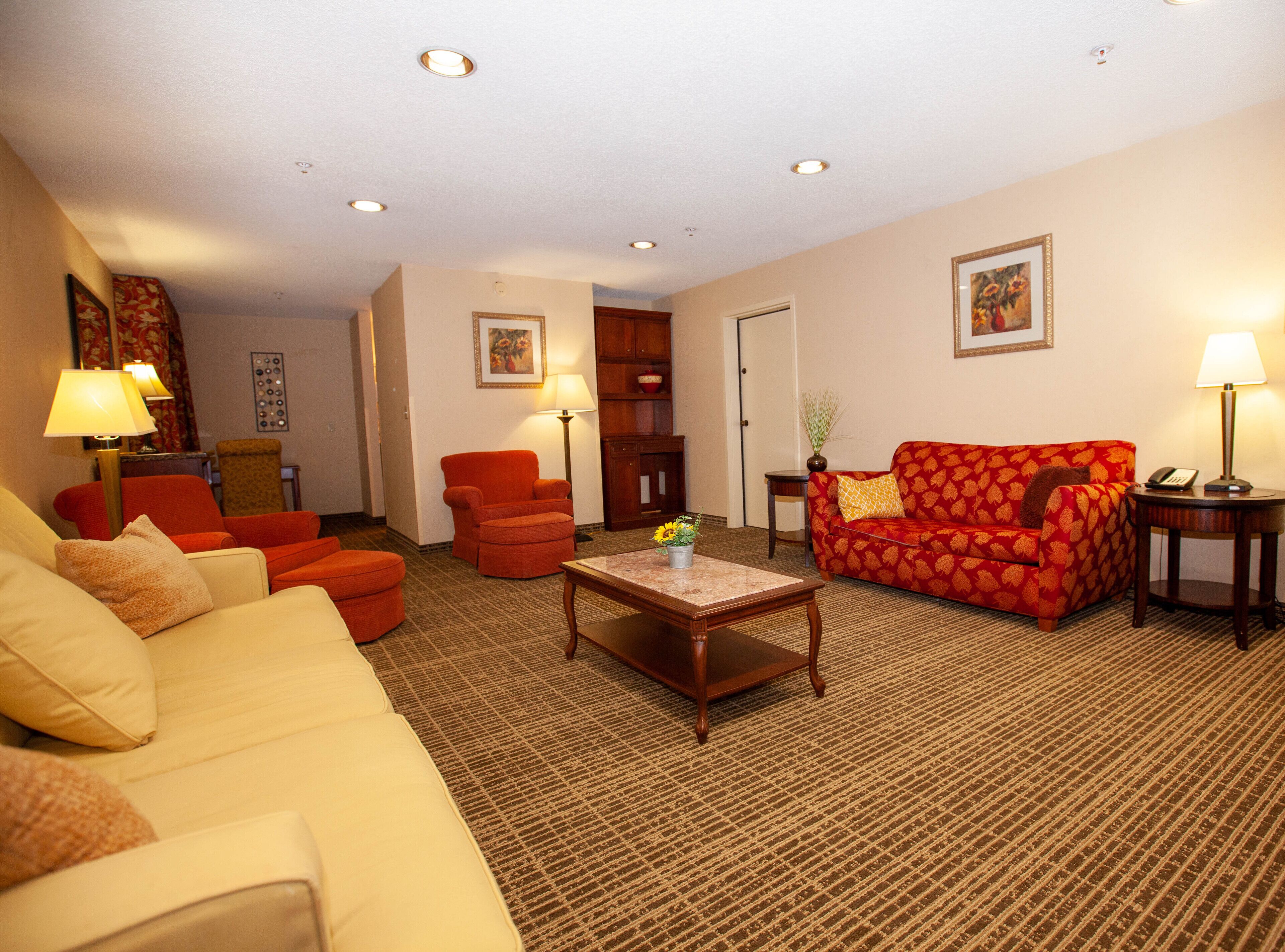 A living room with a beige sofa, red armchair, and patterned red sofa. There is a coffee table with a vase of flowers.