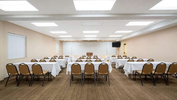 A conference room with multiple tables and chairs, carpeted floor, and a white ceiling with lights.