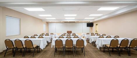 A conference room with multiple tables and chairs, carpeted floor, and a white ceiling with lights.