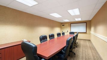 Une salle de conférence avec une longue table en bois, six chaises noires, un tableau blanc et un écran de projection.