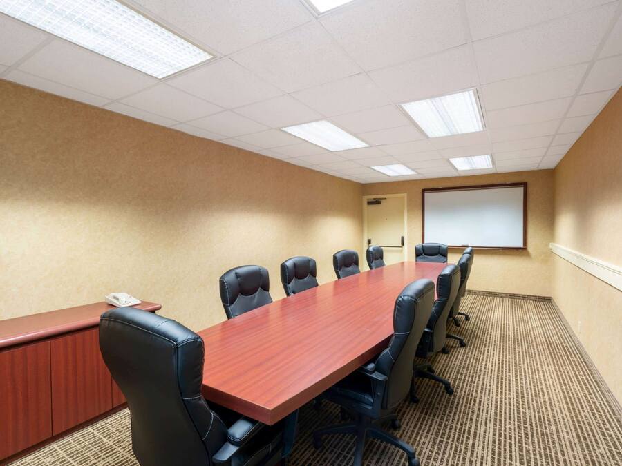 Une salle de conférence avec une longue table en bois, six chaises noires, un tableau blanc et un écran de projection.