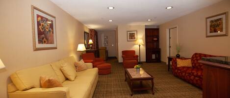 A living room with a beige sofa, red armchairs, a wooden coffee table, and a patterned carpet.