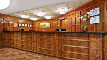 A reception area with a wooden reception desk, framed certificates on the wall, and a sign indicating check-in and check-out times.