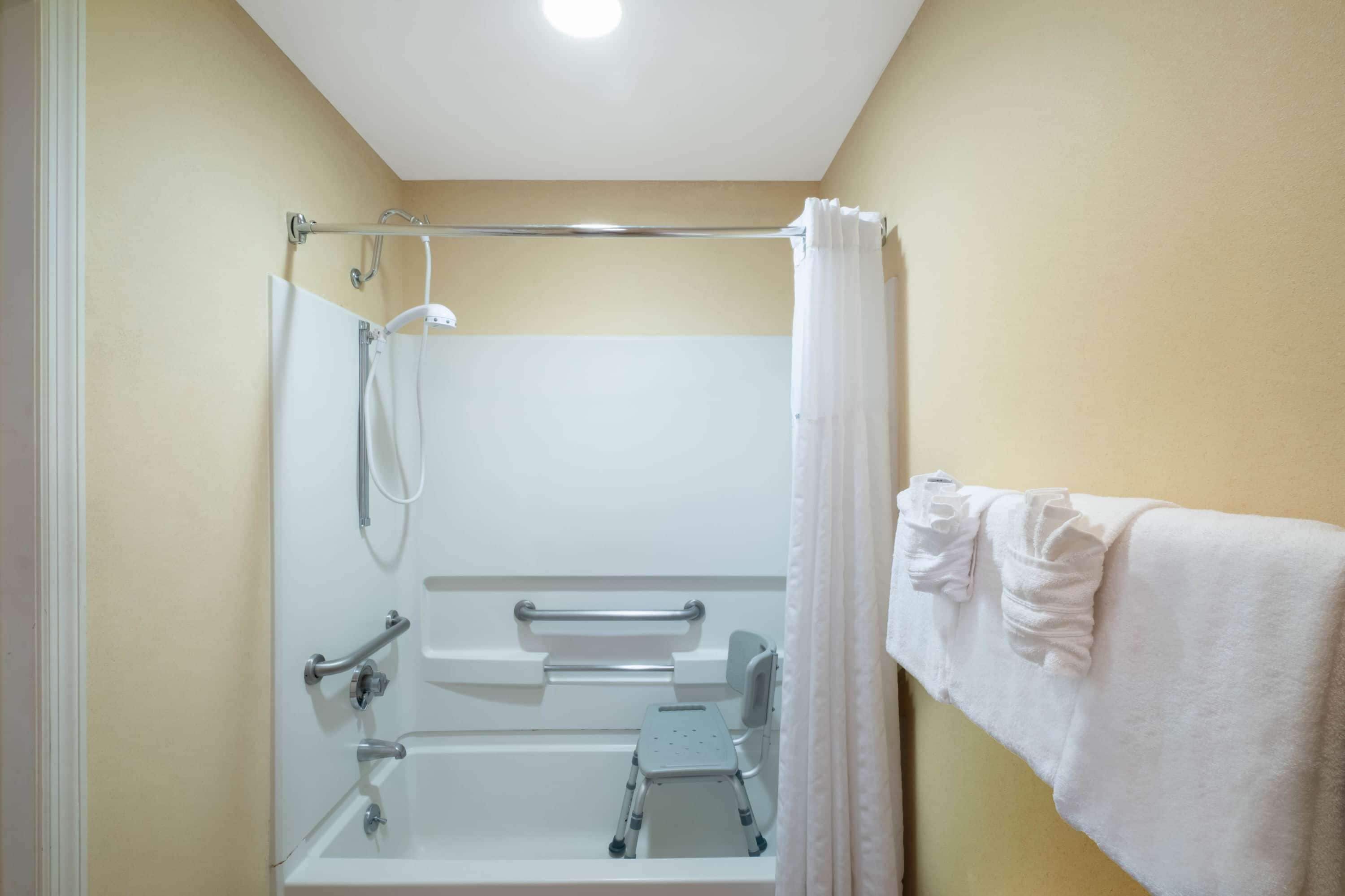 A bathroom with a shower, grab bars, a wheelchair-accessible bench, and a towel rack.