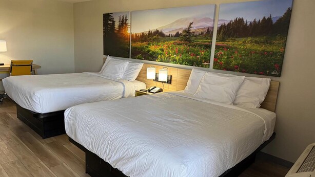 A hotel room with two beds, a nightstand with a lamp, and a painting of a landscape on the wall. - Days Inn by Wyndham Reno (Reno)