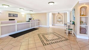 A hotel lobby with a reception desk, a black doormat, a patterned rug, and a seating area with a chair and a table. - Days Inn by Wyndham Reno (Reno)