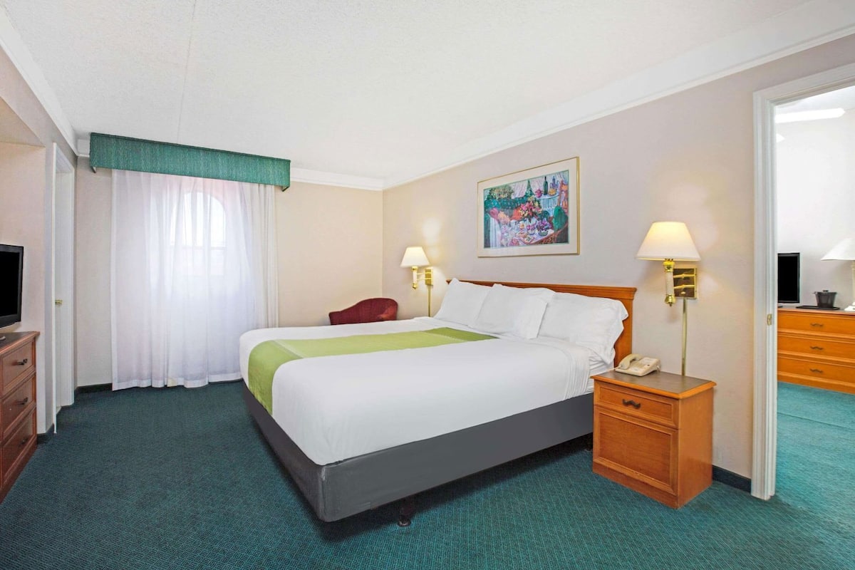 A hotel room with a bed, bedside lamps, a desk with a phone, a television, and a painting on the wall.