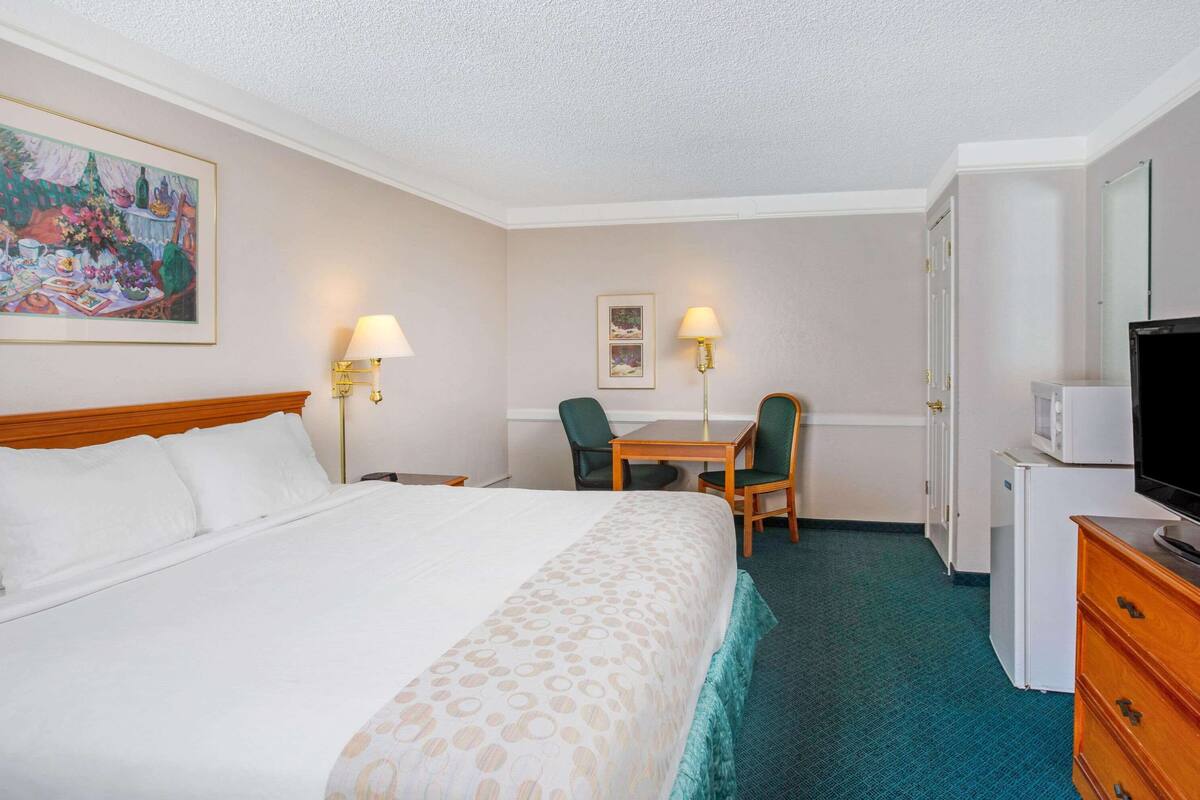 A hotel room with a bed, a desk, two chairs, a television, and a refrigerator.