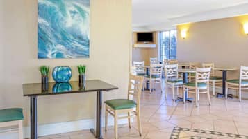A dining area with a table and chairs, a painting on the wall, and a television above the table.