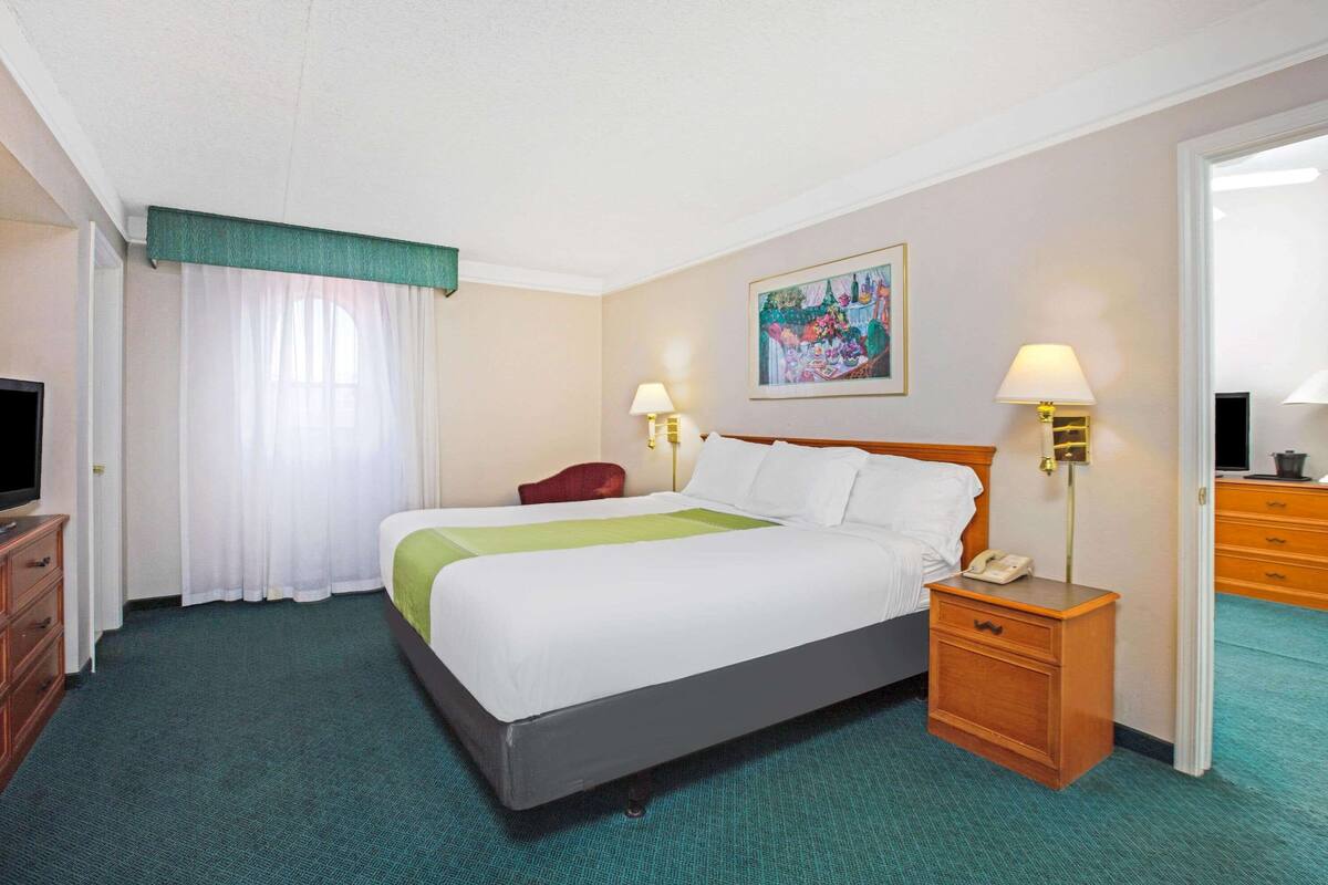 A hotel room with a bed, two bedside tables, a TV, a desk, and a chair.