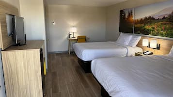 Quarto de hotel com duas camas, uma escrivaninha com cadeira, televisão e um quadro na parede.