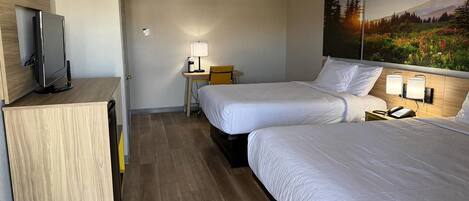 A hotel room with two beds, a desk with a chair, a TV, and a painting on the wall.