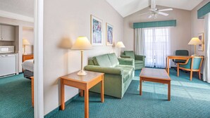 A hotel room with a green sofa, two wooden side tables, a wooden desk, a ceiling fan, and a window with curtains. - Days Inn by Wyndham Reno (Reno)